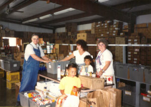 Food Pantry Director Fran Botzin (R) sorting food with volunteers Arden Wood (L) and Jayne James (Center) and children in 1994.